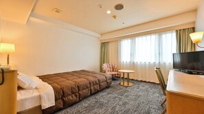 Habitació d'hotel amb llit, escriptori amb televisió, cadira, taula petita i finestra amb cortines.