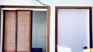 Una habitació amb una porta corredissa, una porta blanca, una estant amb objectes decoratius i una planta.