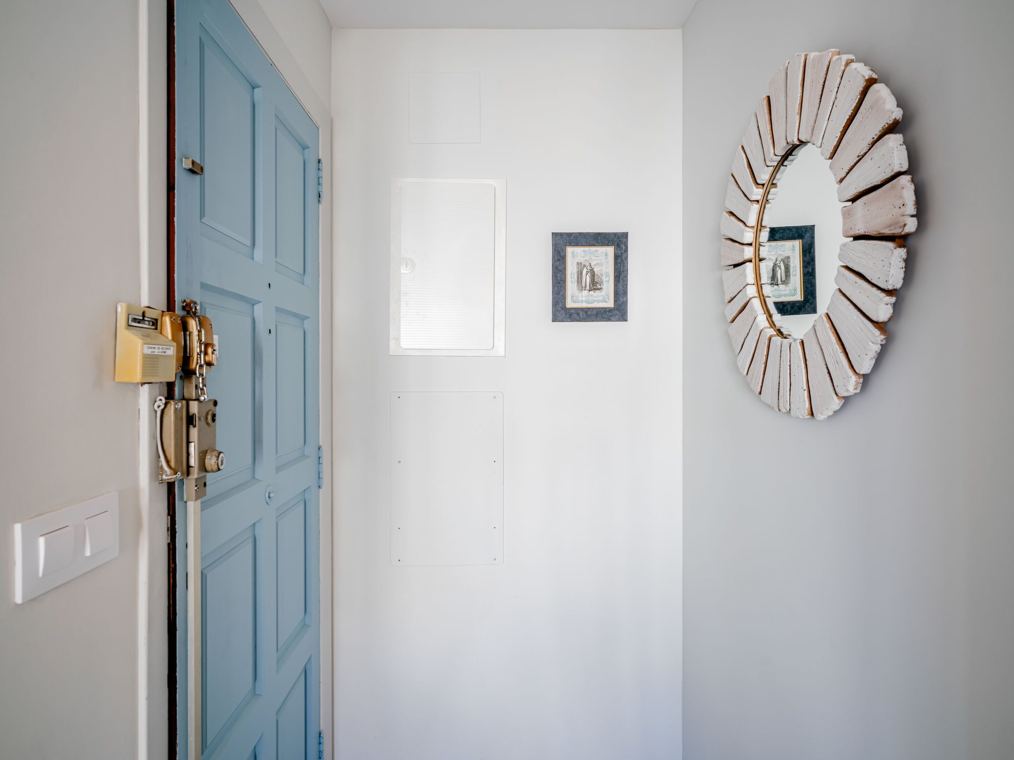 A door with a blue handle, a white wall with two framed pictures, and a circular wall decoration.