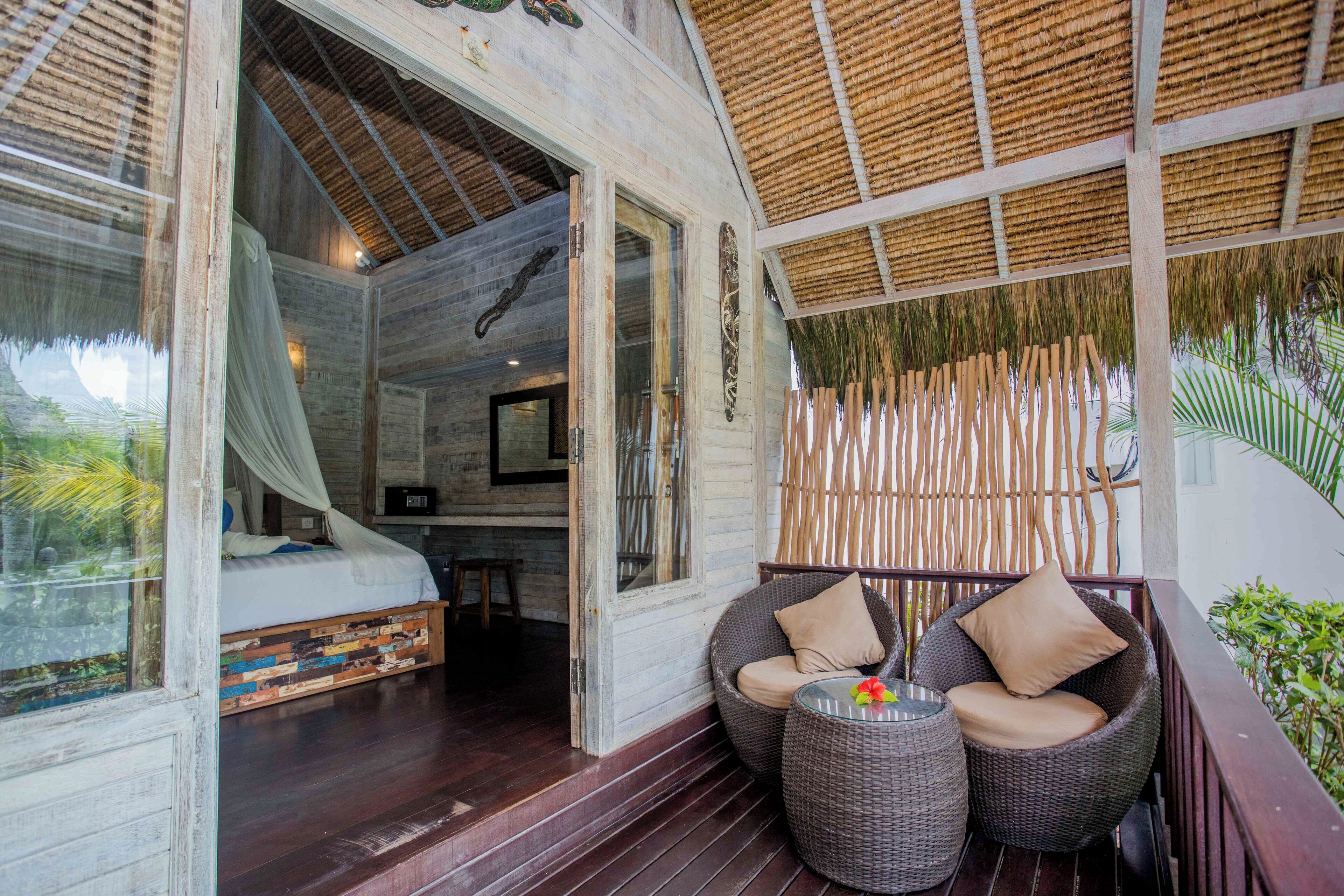 A wooden room with a bed, a wicker chair, and a small table.