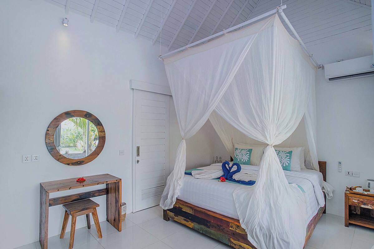 A bedroom with a four-poster bed, a wooden desk, and a mirror on the wall.