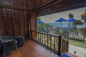 Un terrazzo in legno con mobili in vimini, vista sul mare e ombrelloni blu.