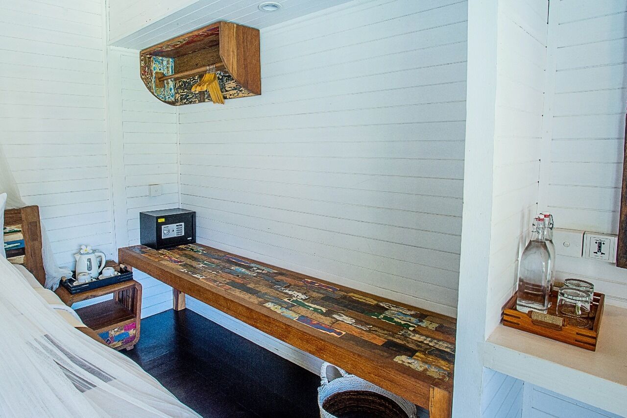 A small, cozy room with a wooden bench, a microwave, and a shelf with a bottle and glasses.