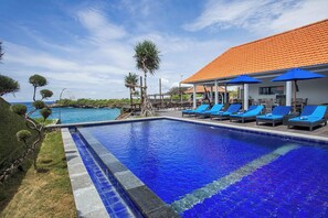 A swimming pool with blue tiles, lounge chairs, and a building with a tiled roof. - Water Blow Huts (Lembongan Island)