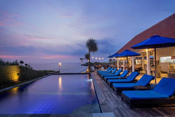 A poolside area with lounge chairs and umbrellas, overlooking a body of water at dusk. - Water Blow Huts (Lembongan Island)