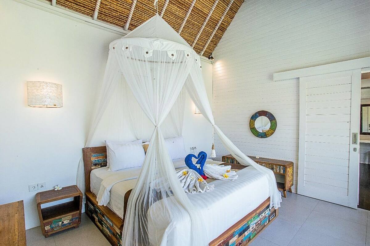 A bed with a canopy, a bedside table, a wall-mounted light, and a door.