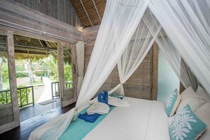 A bedroom with a canopy bed, a view of the garden, and a wooden floor. - Water Blow Huts (Lembongan Island)