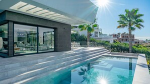 A modern house with a glass-enclosed patio, a swimming pool, and a view of palm trees and other houses. - Vacation home Leda by Interhome (Jávea)