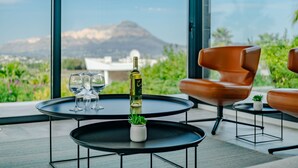 A modern outdoor seating area with two round tables, one with a bottle of wine and glasses, and a mountain view in the background. - Vacation home Leda by Interhome (Jávea)