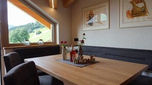 A dining area with a wooden table, chairs, and a bench. There are framed artworks on the wall and a window with a view of a green landscape. - Apartment in Kaunerberg Near Ski Resort (Kaunerberg)