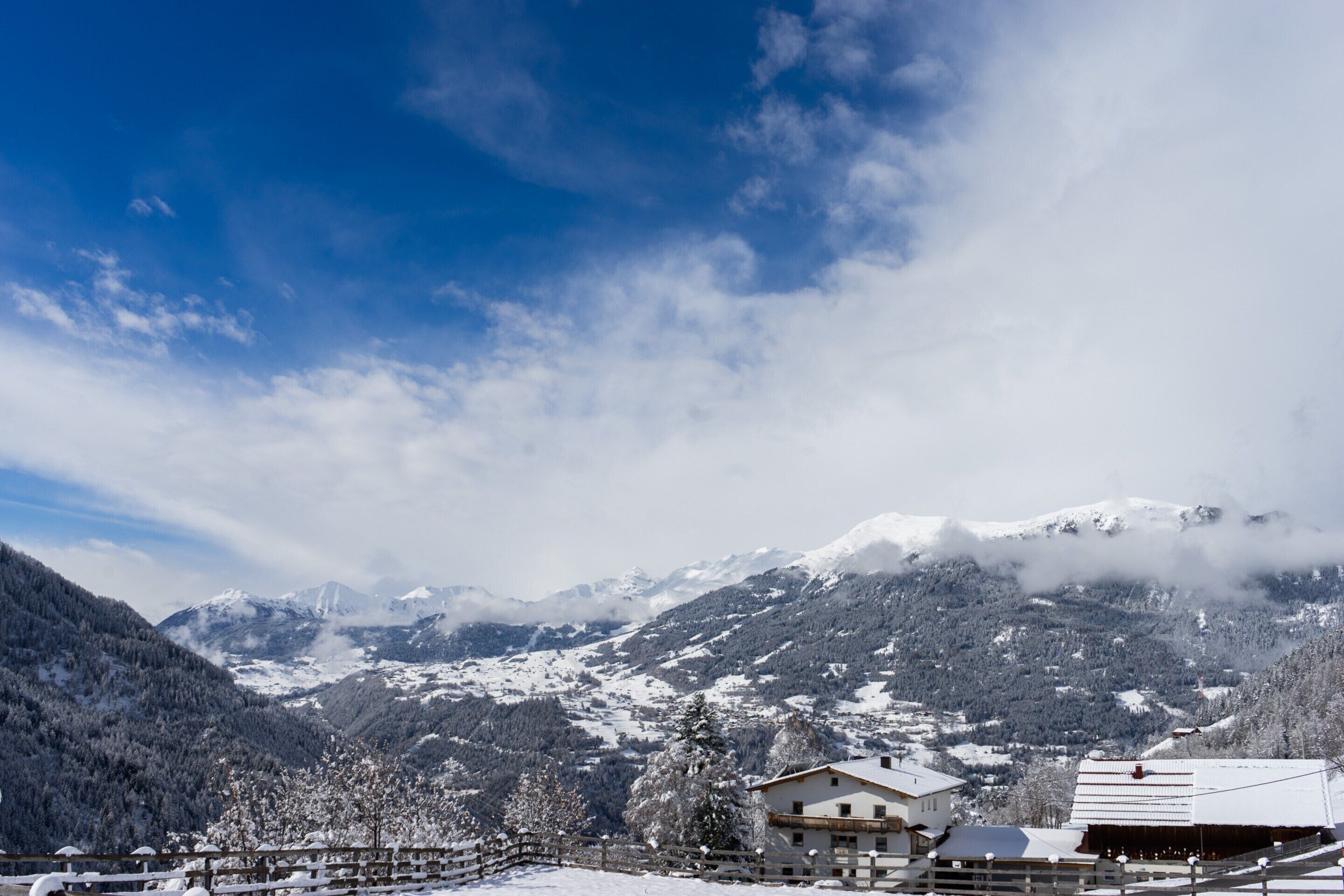 A snow-covered mountain landscape with a chalet-style building in the foreground, surrounded by trees and mountains.
