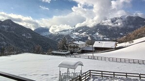 Een besneeuwd landschap met een berg op de achtergrond, een gebouw met schuin dak en een besneeuwde omheining.
