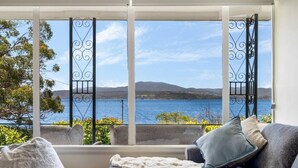 Habitación con vista a un lago y colinas, un sofá gris con una manta, y una ventana con barrotes.