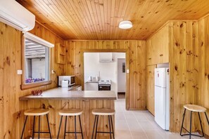 A wooden interior with a kitchen area, bar stools, and a refrigerator. - Lemonade by the Beach: Serene Huon Valley Retreat with Water Views (Police Point)