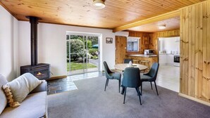 Un interior acogedor con una estufa de leña, un comedor con sillas y una cocina visible a través de una puerta abierta.