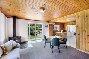 A cozy interior with a wood-burning stove, a dining area with chairs, and a kitchen visible through an open door. - Lemonade by the Beach: Serene Huon Valley Retreat with Water Views (Police Point)