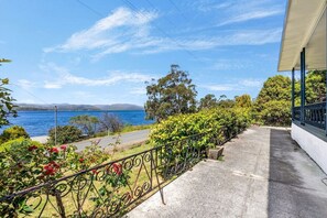 A balcony with a view of a lake and mountains, surrounded by greenery and a metal railing. - Lemonade by the Beach: Serene Huon Valley Retreat with Water Views (Police Point)