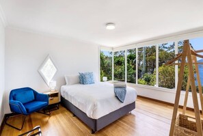 Un dormitorio con una cama grande, una silla azul, una escalera de madera y vistas a árboles y agua.