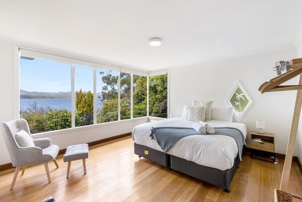 A bedroom with a large bed, a chair, a small table, and a view of the sea.