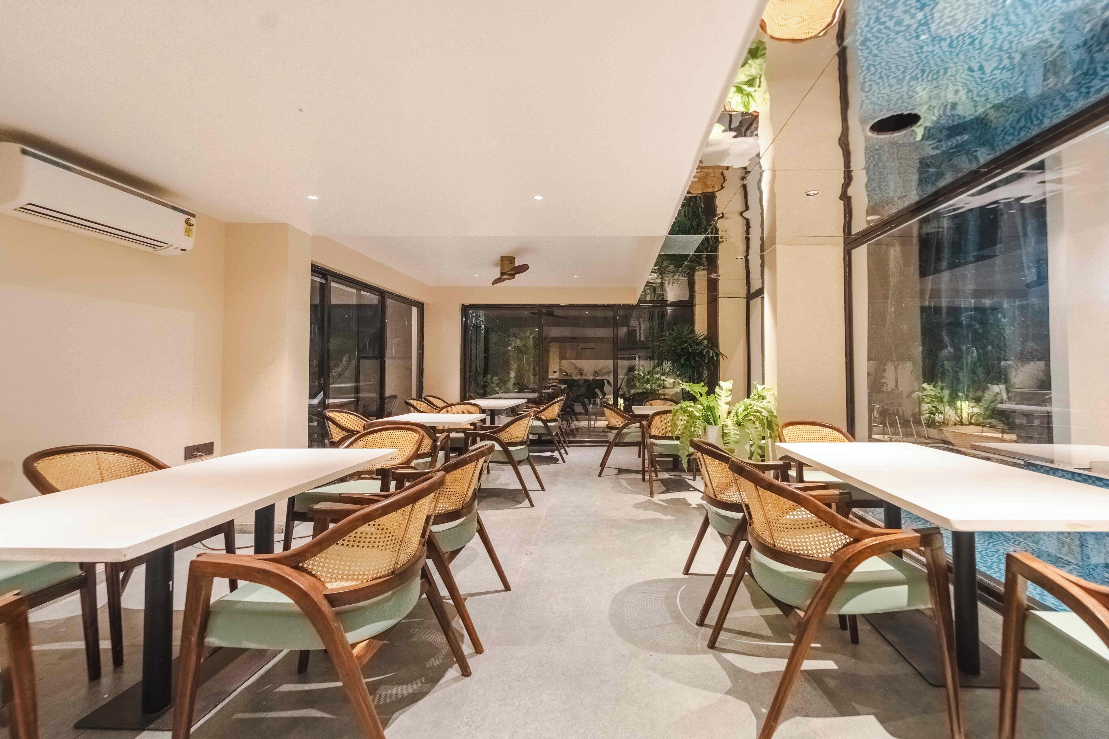 A restaurant with multiple tables and chairs, indoor plants, and large windows.
