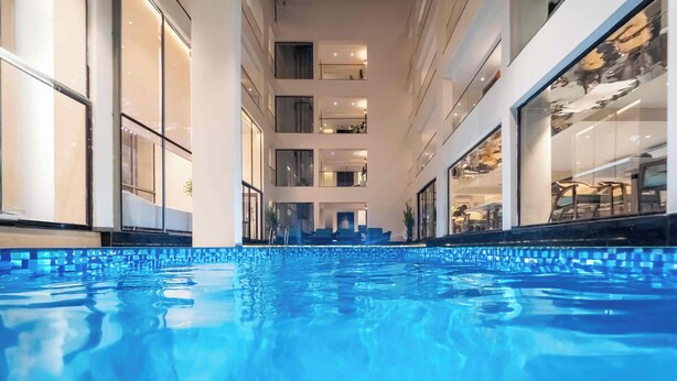 A swimming pool with a clear view of the building's interior, including multiple floors and balconies. - Vilmaris Luxury Hotel in Calangute (Calangute)