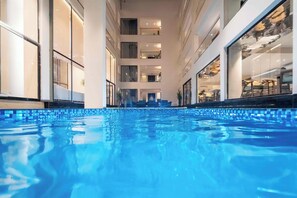 A swimming pool with a clear view of the building's interior, including multiple floors and balconies. - Vilmaris Luxury Hotel in Calangute (Calangute)