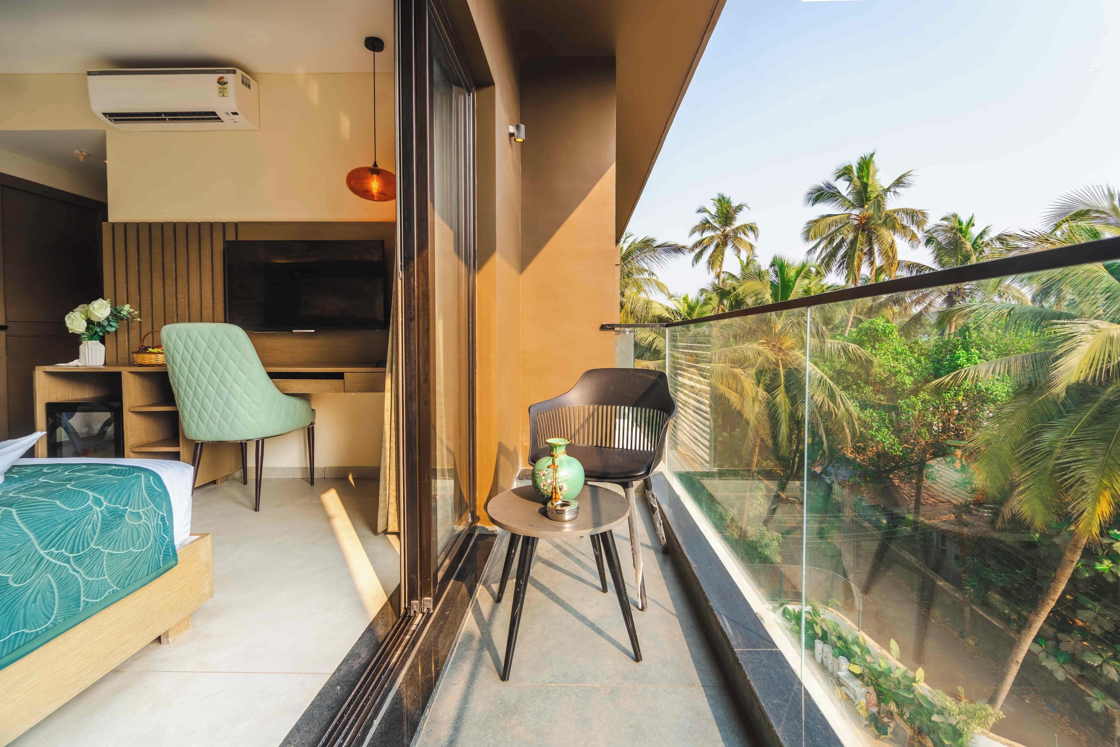 Un balcon avec vue sur les palmiers, un lit, un bureau avec une chaise et un téléviseur.