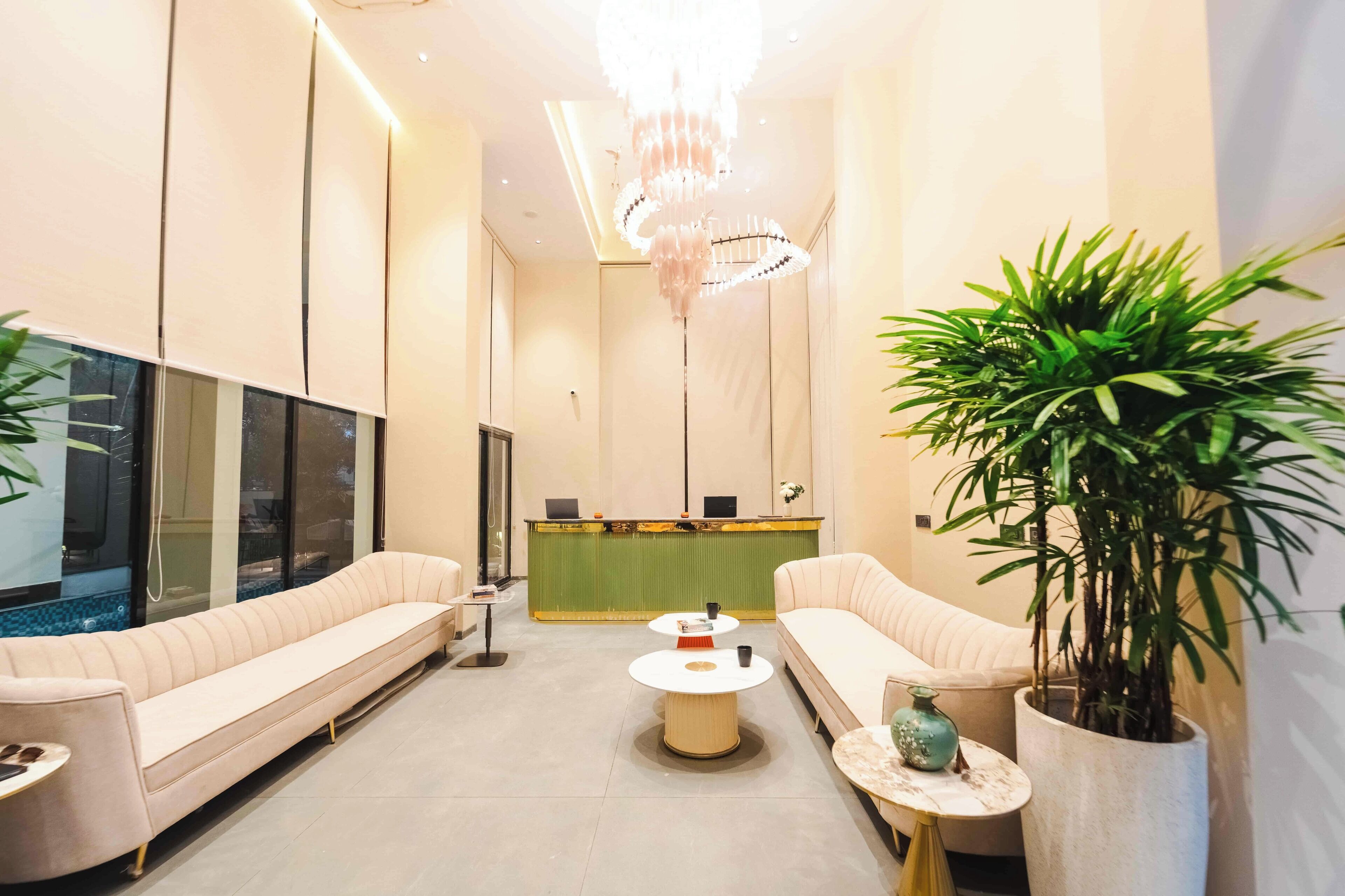 Een moderne loungeruimte met een bank, een receptiebalie, een kroonluchter en potplanten.