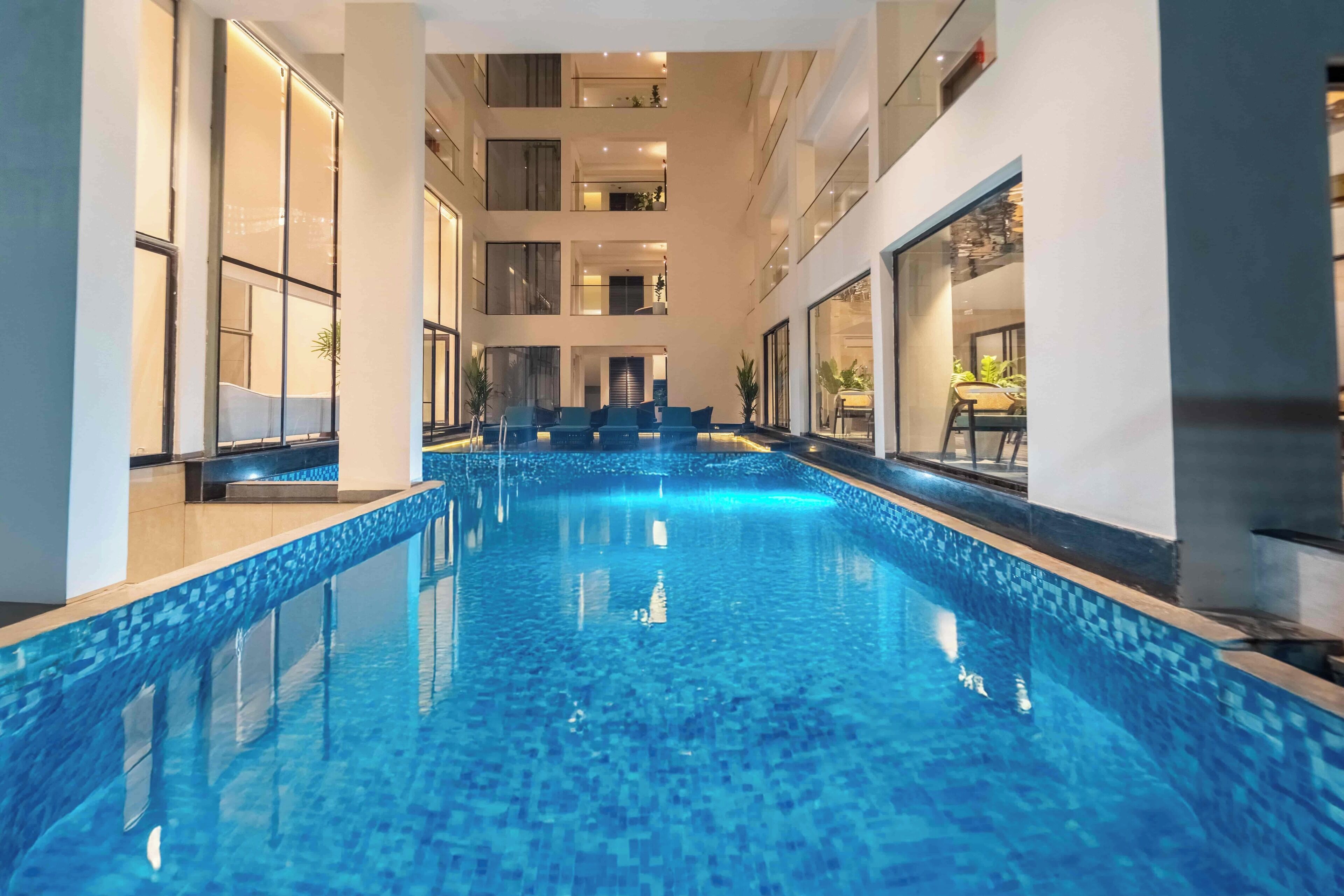 A modern indoor swimming pool with a tiled floor and walls, surrounded by balconies and windows.