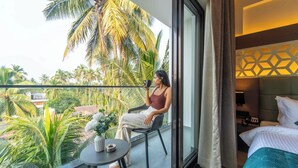 Un balcon avec vue sur les palmiers et une chambre d’hôtel avec un lit et une table de chevet.