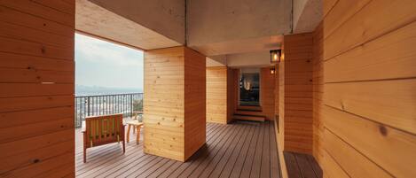 Una terraza de madera con un banco y una mesa, que conduce a un balcón con vistas.