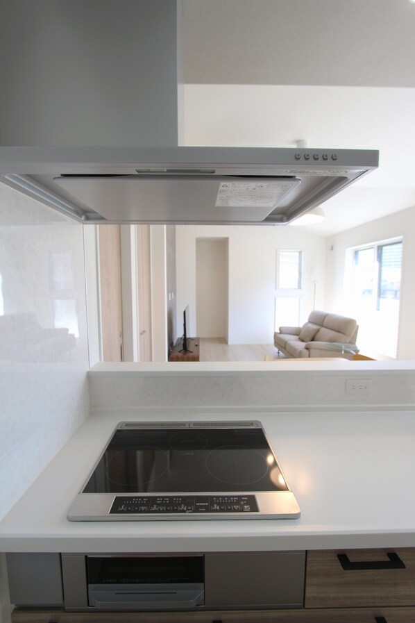 A modern kitchen with a built-in induction cooktop, a stainless steel range hood, and a white countertop.