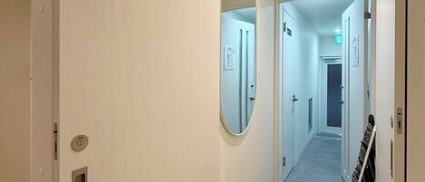 A hallway with a wooden floor, white walls, and a mirror on one wall.