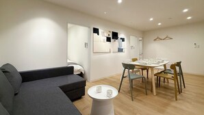 Una sala de estar moderna con un sofá gris, una mesita redonda con dos tazas blancas, y un comedor con una mesa y sillas de madera.