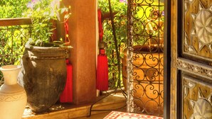 A balcony with a wrought iron gate, potted plants, and a view of the surrounding greenery. - Riad Roxanne (Marrakech)