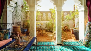 A Moroccan-style interior with a patterned floor, a seating area with cushions and a table, and potted plants. - Riad Roxanne (Marrakech)