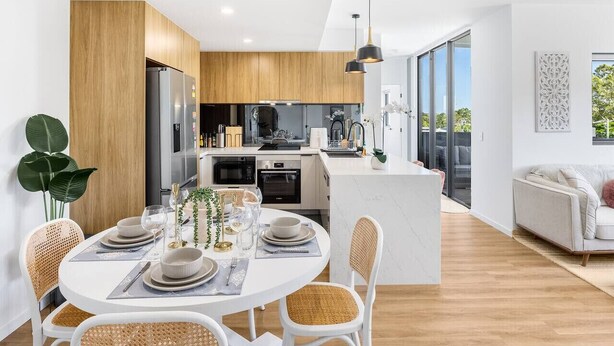 A modern kitchen with a central island, a dining area with a round table, and a living space with a sofa.