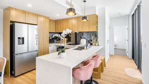 A modern kitchen with a central island, stainless steel appliances, wooden cabinets, and pink bar stools.