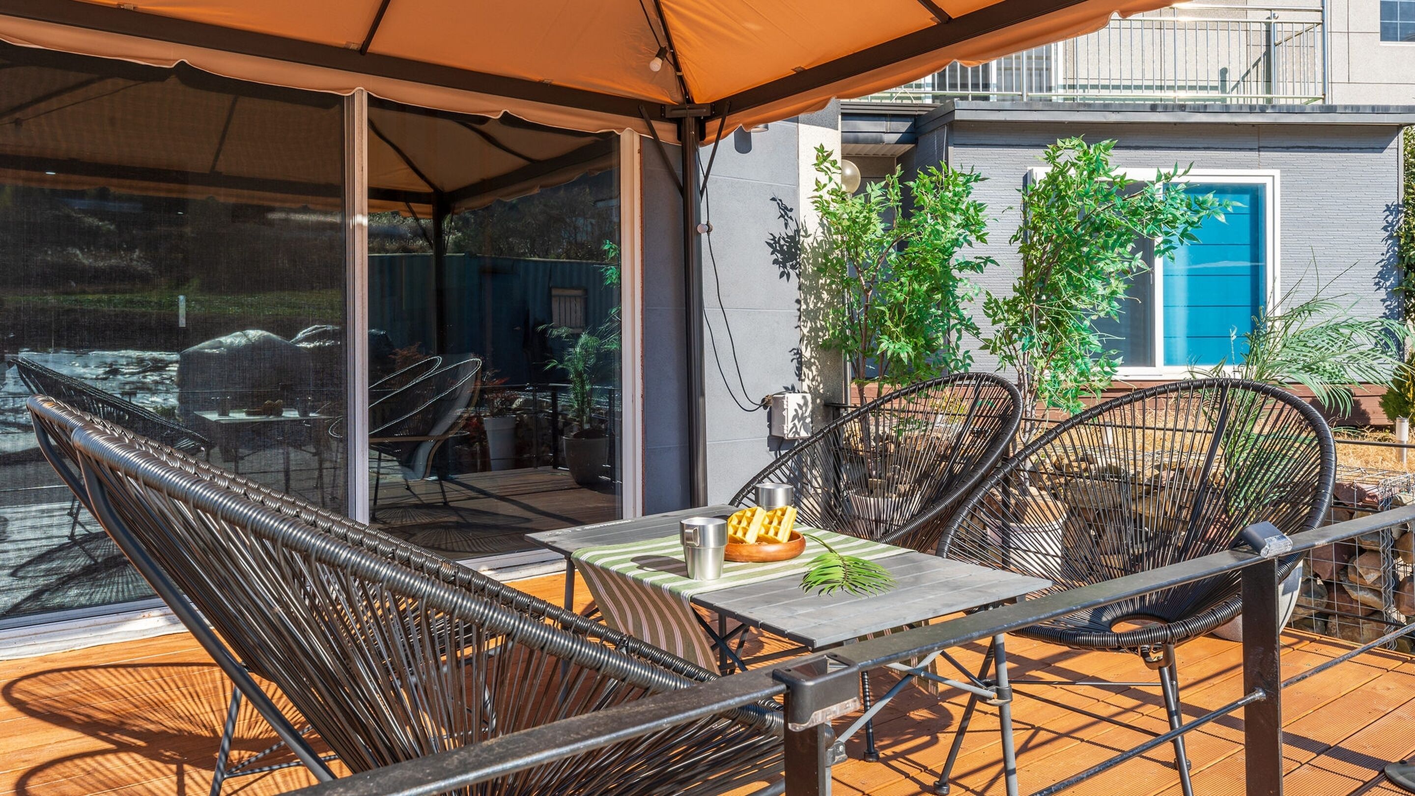 Um pátio externo com mesa e cadeiras, uma área de estar coberta e vista para um edifício com porta azul.