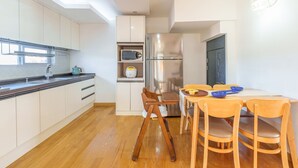 Une cuisine moderne avec des meubles blancs, un réfrigérateur en acier inoxydable et une table à manger en bois, assortie de chaises.
