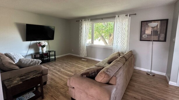 Una sala de estar con sofá, televisor, lámpara de pie y ventana con cortinas.