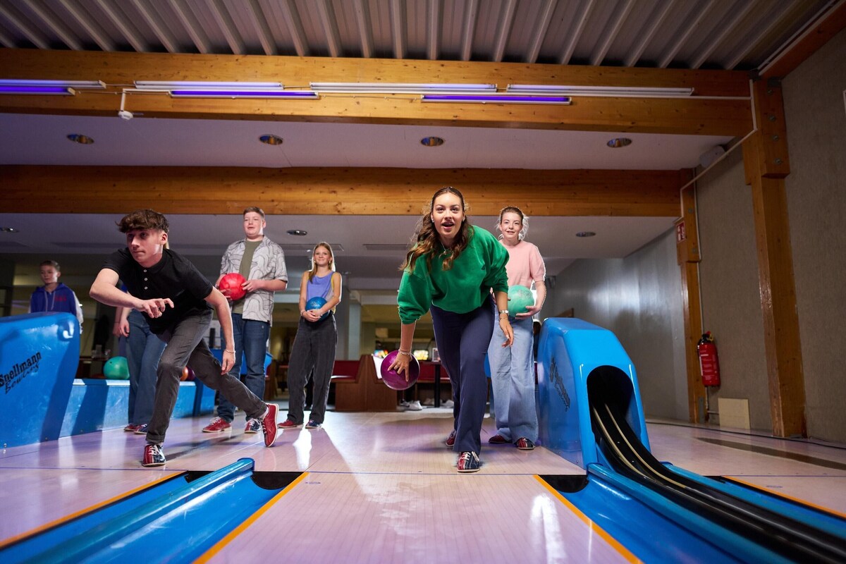 A bowling alley with wooden beams on the ceiling, a blue bowling lane, and people bowling.