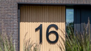 En byggnad med ett stort siffran "16" på en träpanel, en tegelvägg och ett fönster.