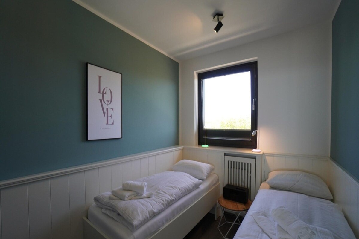 Un dormitorio con dos camas individuales, un radiador, una ventana y un cuadro en la pared.