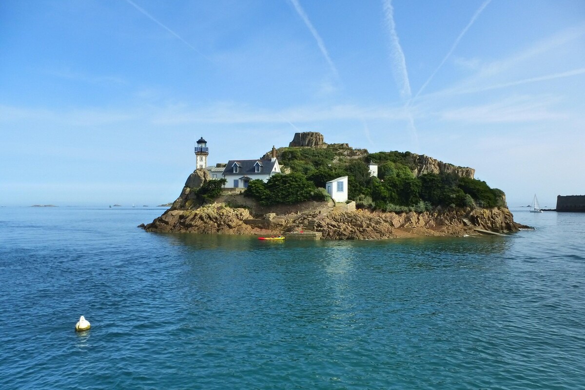 A coastal building with a lighthouse, situated on a rocky island with a clear view of the sea.