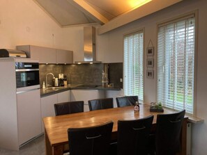 A modern kitchen with a dining area, featuring a built-in oven, stainless steel appliances, and a large wooden table with chairs.