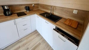 Egy kis méretű konyha fehér szekrényekkel, fekete mosogatóval, kávéfőzővel és mosogatógéppel.