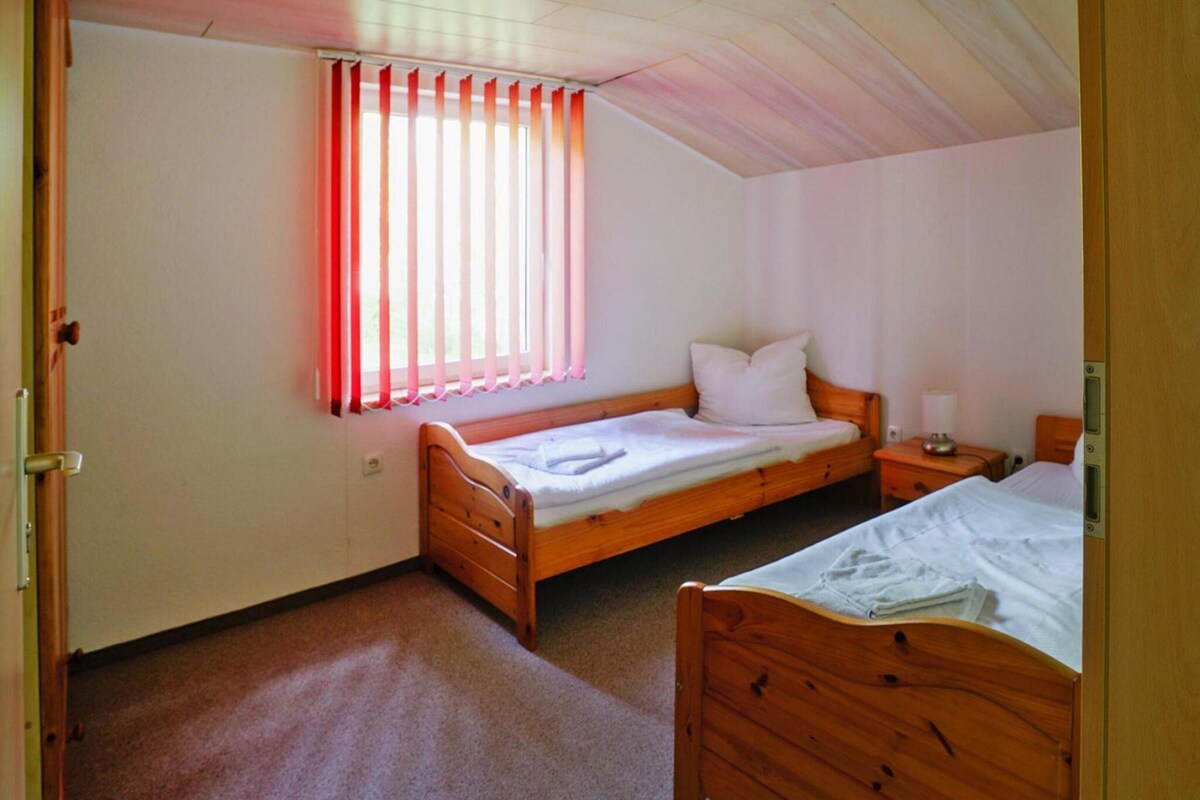 Ein Schlafzimmer mit zwei hölzernen Betten, einem Fenster mit roten Vorhängen und einer Holzbalkendecke.