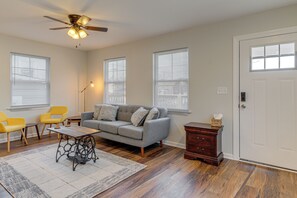 Ein Wohnzimmer mit grauem Sofa, gelben Sesseln, Couchtisch und Deckenventilator.