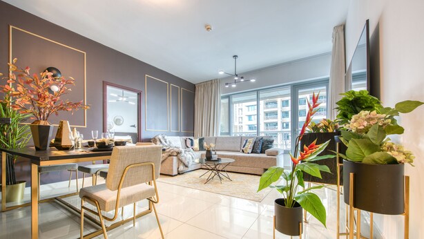 Ein modernes Wohnzimmer mit Sofa, Couchtisch und Sesseln. Pflanzen und ein an der Wand befestigter Fernseher sind ebenfalls vorhanden.